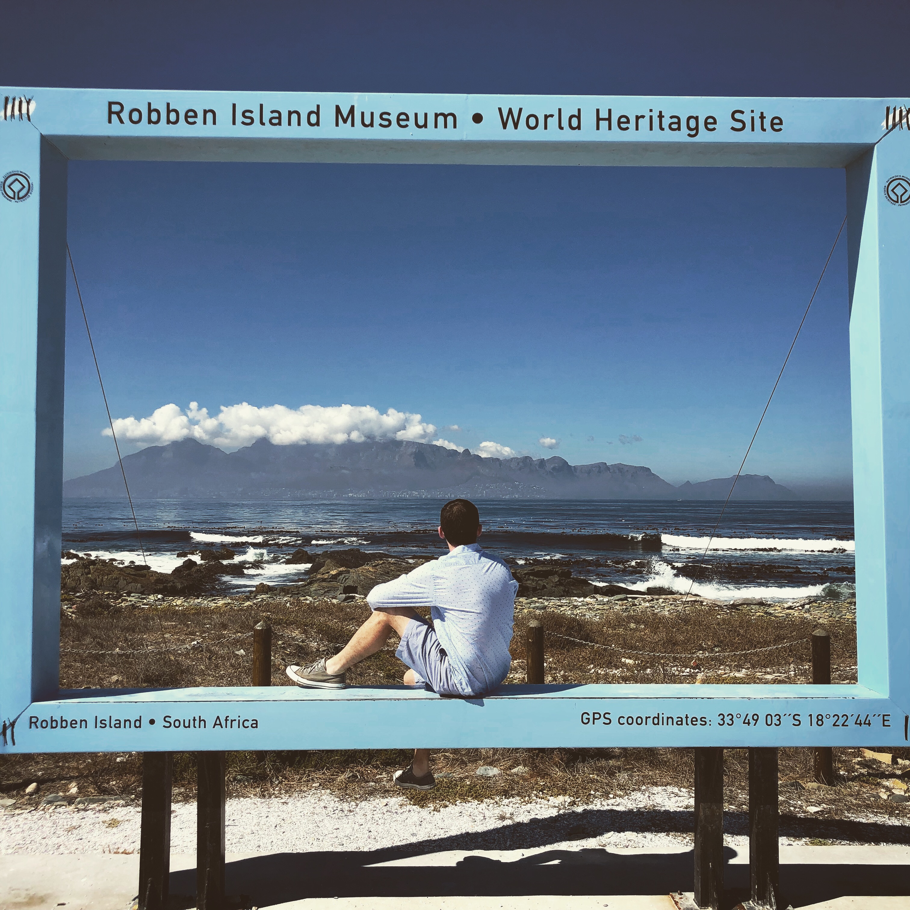Peter seated inside a Robben Island photo frame with Table Mountain beyond the water.